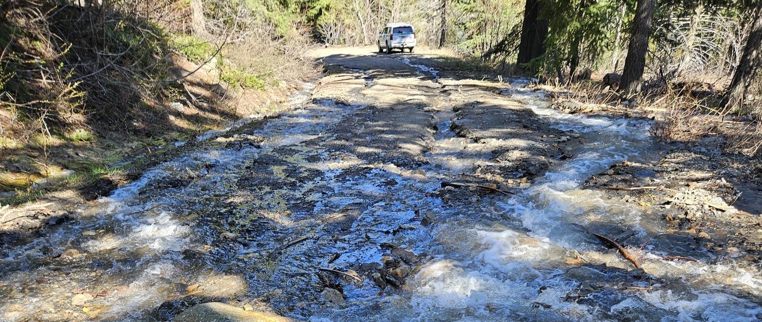 A car drives away on a road covered in running water