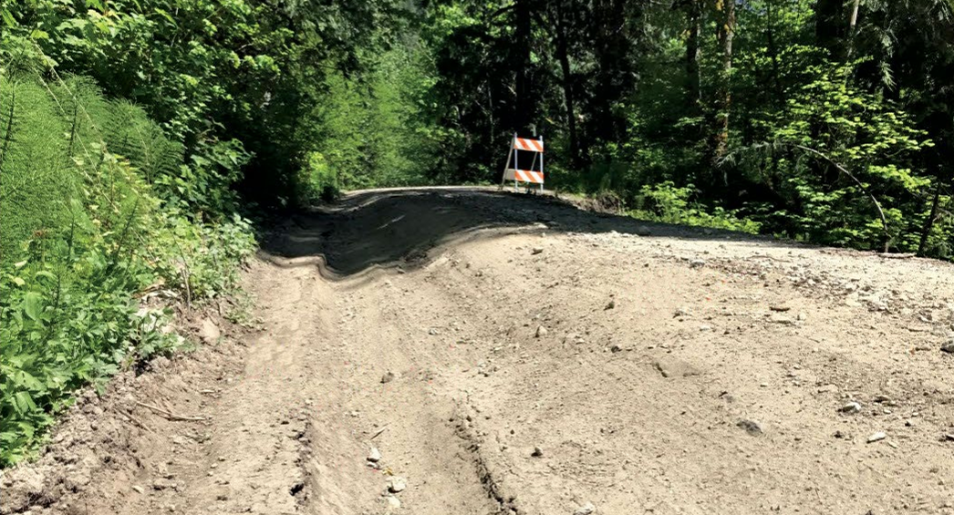 Road with a deep ditch on one side and an orange-striped caution easel on the other side