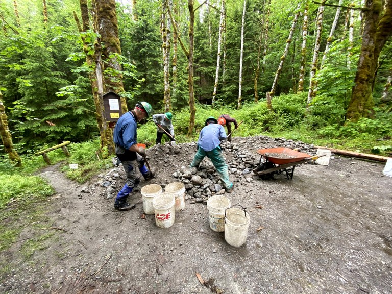 Several volunteers shovel gravel beside a trail.