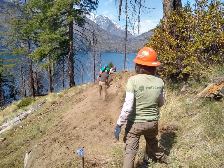 A volunteer looks out over a lake view while the crew does trail work.