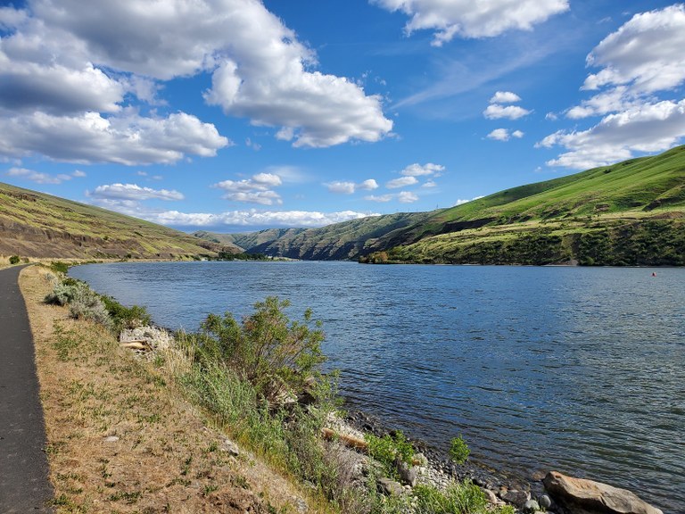 Snake River Trail (Boyer Park Bluff) Photo by Aaron Czechkowski. A paved trail along the Snake River under blue sky and puffy clouds.