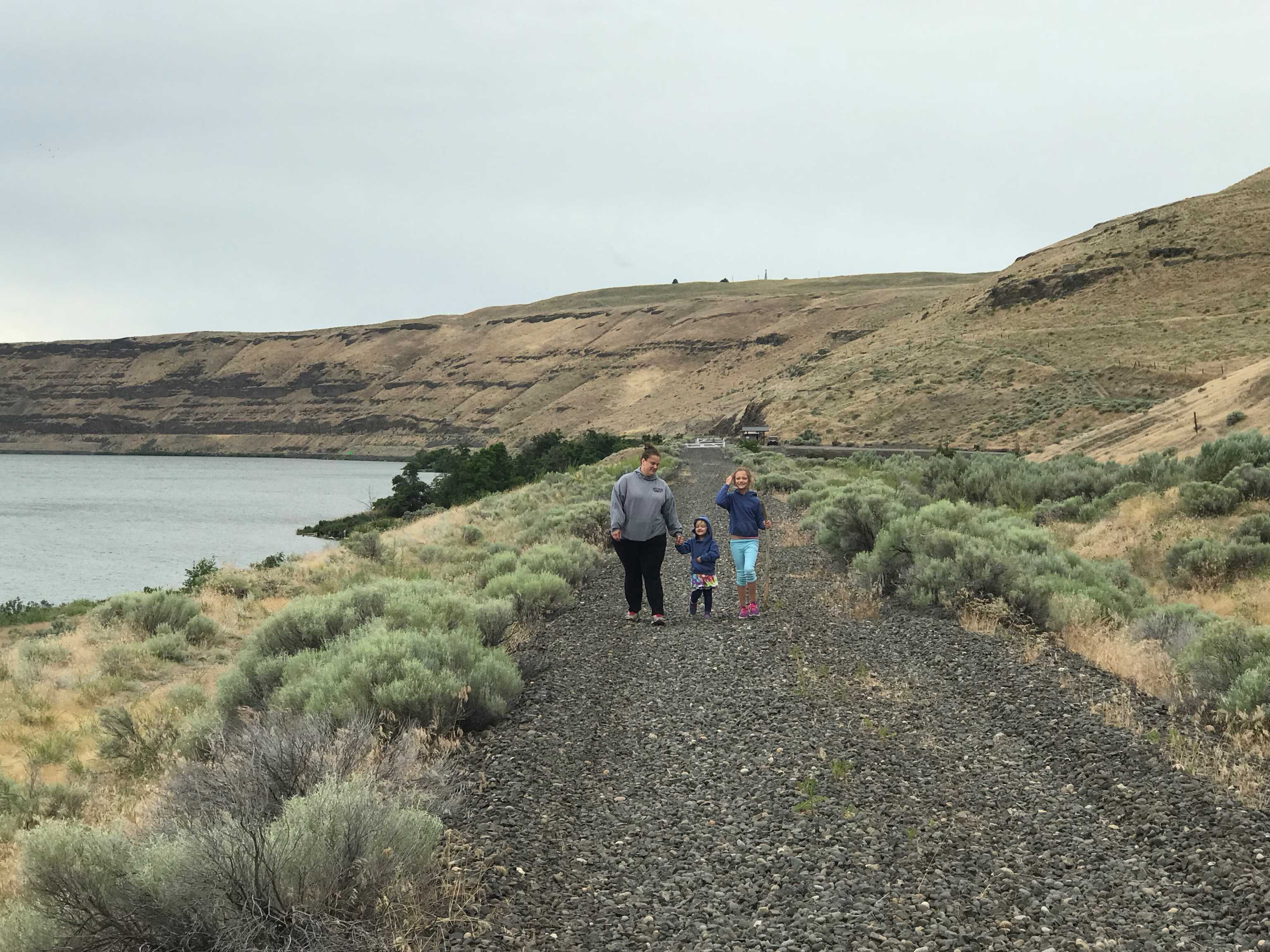 An adult with two kids hiking on the Columbia Plateau Trail - Snake River with water in the background. Photo by Happydiaz.