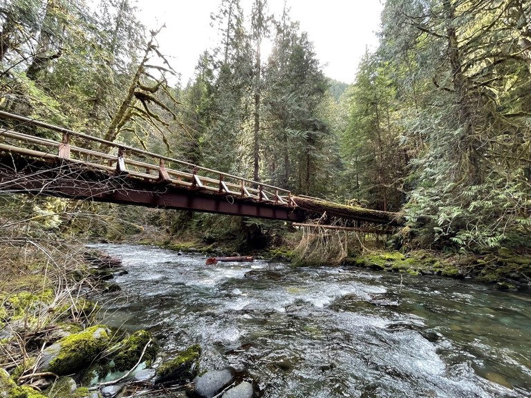 A large wood bridge crosses a rushing river under a gray sky 
