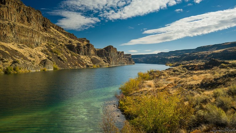 Deep lake surrounded by dry grasses and a rocky promontory. Photo by demonstrate.