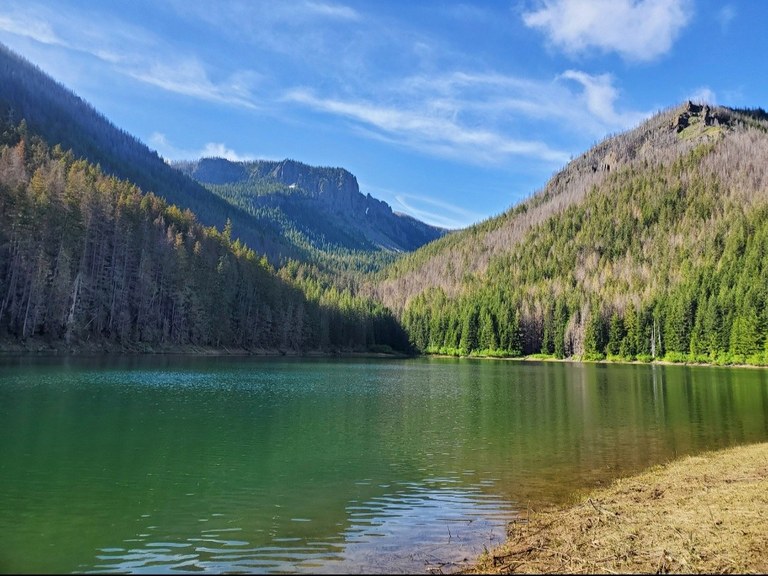 An aquamarine lake surrounded by forest and a rocky outcropping in the distance. Photo by KZMoves. 