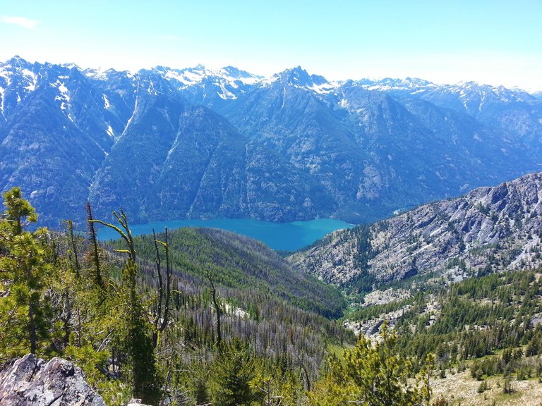 View from a high ridge looking down at Lake Chelan and across to a ridge of mountains rising from the lakeshore. Photo by Karmot