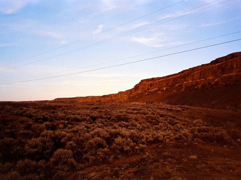 A bluff and some channeled scablands glow red at sunset. 