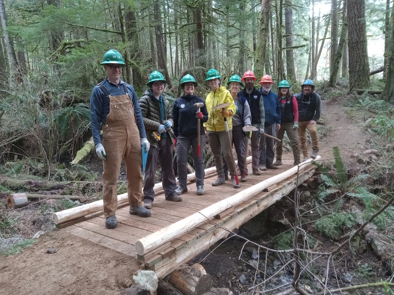 Trail crews in hard hats smile on newly built bridge.