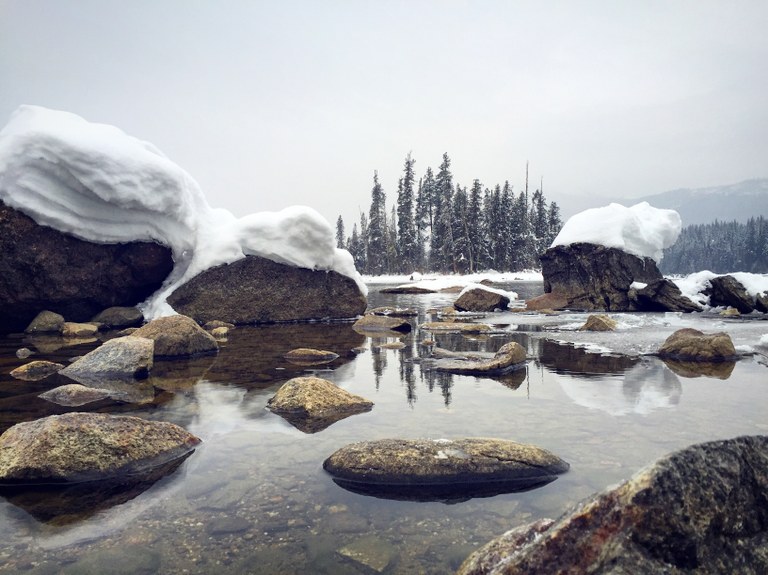 Snowy skies and snow-covered rocks are reflected in the frozen, serene water of Lake Wenatchee.
