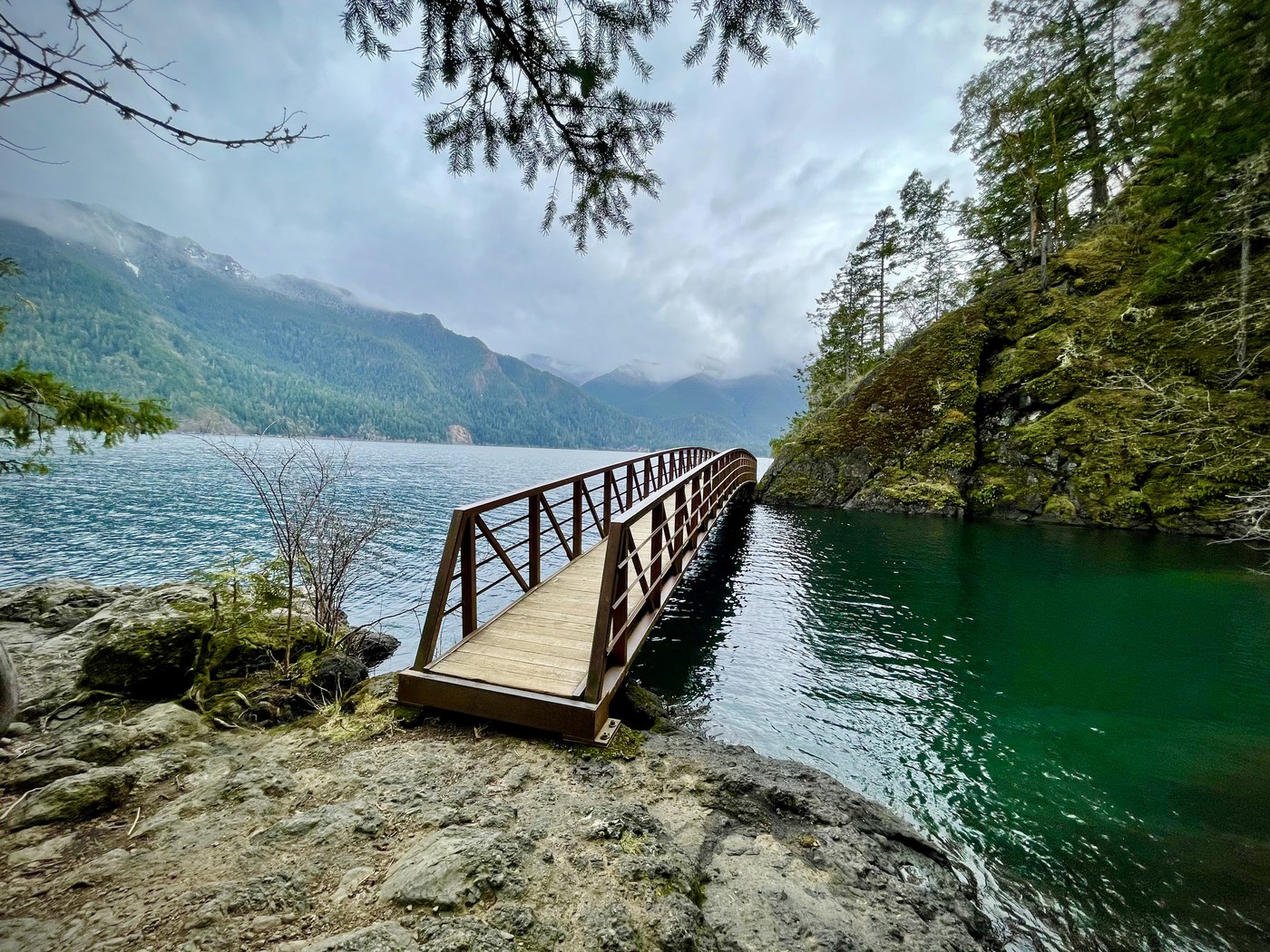 A bridge stretches across a deep blue pool with a large lake beyone. 