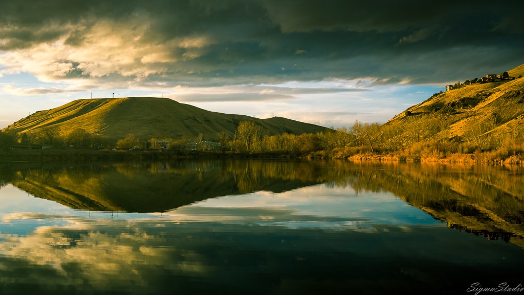 An early morning photo of a calm river with a hill behind.