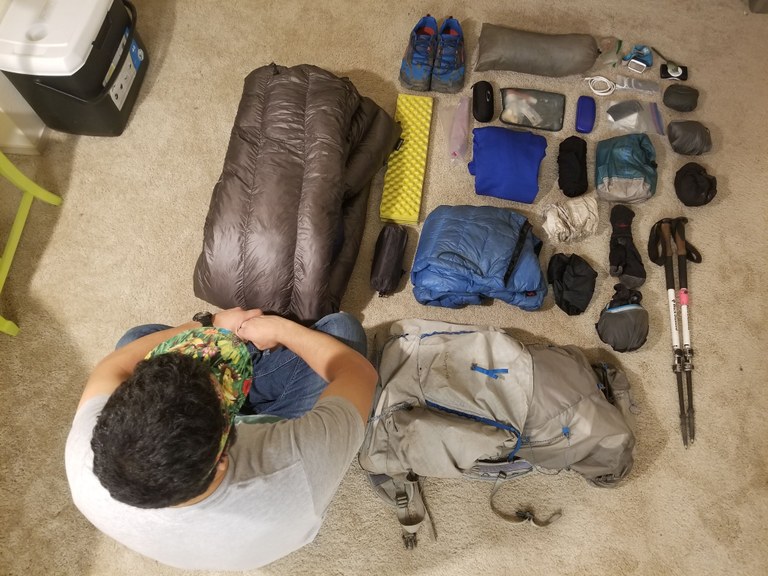 Packing for the Wonderland Trail is a breeze when your gear is organized. Photo by Joseph Gonzalez. A collection of gear is organized on the floor as a hiker looks it over.