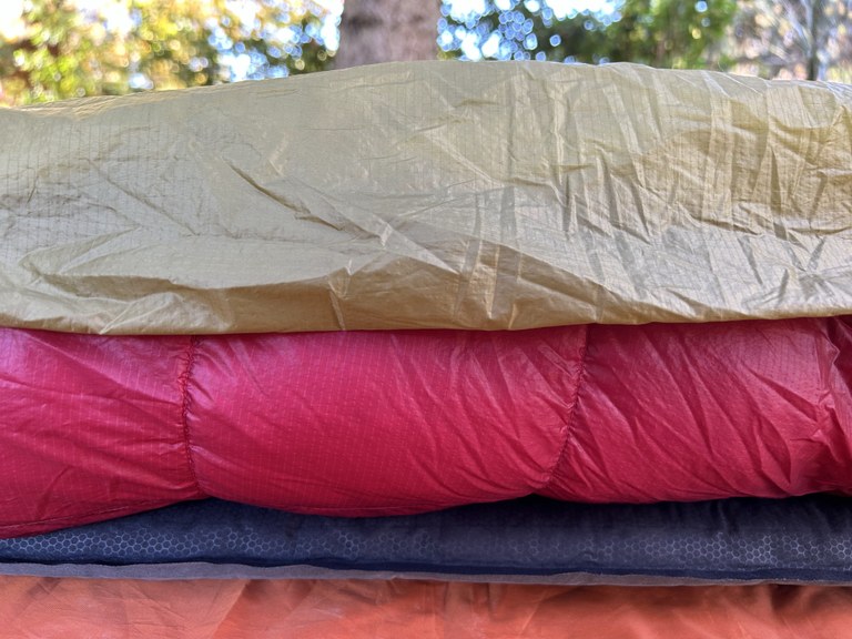 A close-up photo of layers of a ground cloth, a sleeping pad, a sleeping bag and an overquilt.