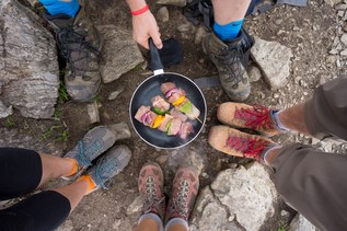 Four hikers stand around a backcountry stove that's cooking dinner.