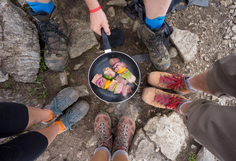 Four pairs of feet surround a pan that's filled with sizzling kabobs.
