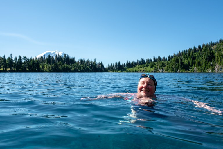 Julie swimming. A woman floats in blue lake water, wearing goggles and a swim cap. 