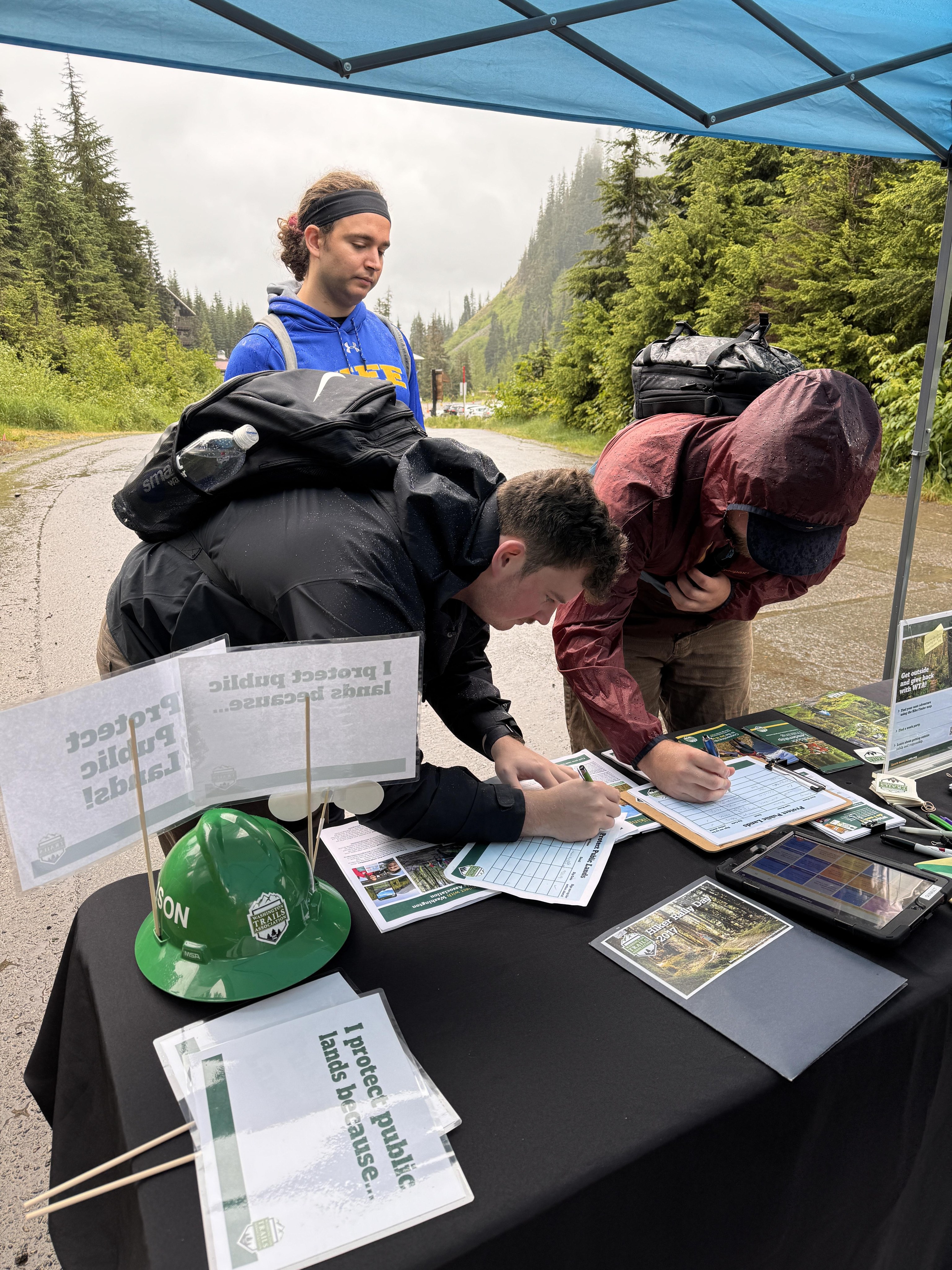 At a trailhead, hikers lean over a table signing a petition