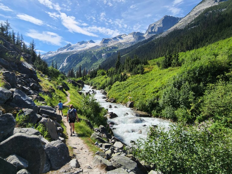 Two hikers walk along a rushing stream.