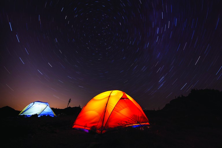 There are a few different ways of illuminating your tent. Consider weight, light distribution and mounting options to decide what's bets for you. Photo by Andres Caldera Two illuminated tents are pitched under a starry night sky.
