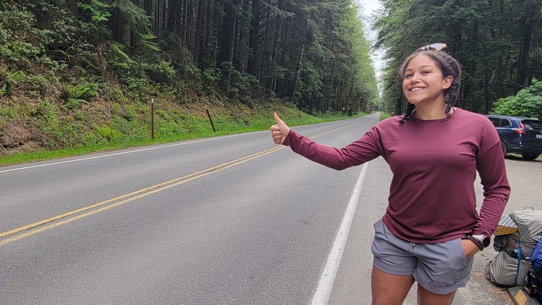 A hiker sticks her thumb out on a road in a national park with hopes of getting a ride.