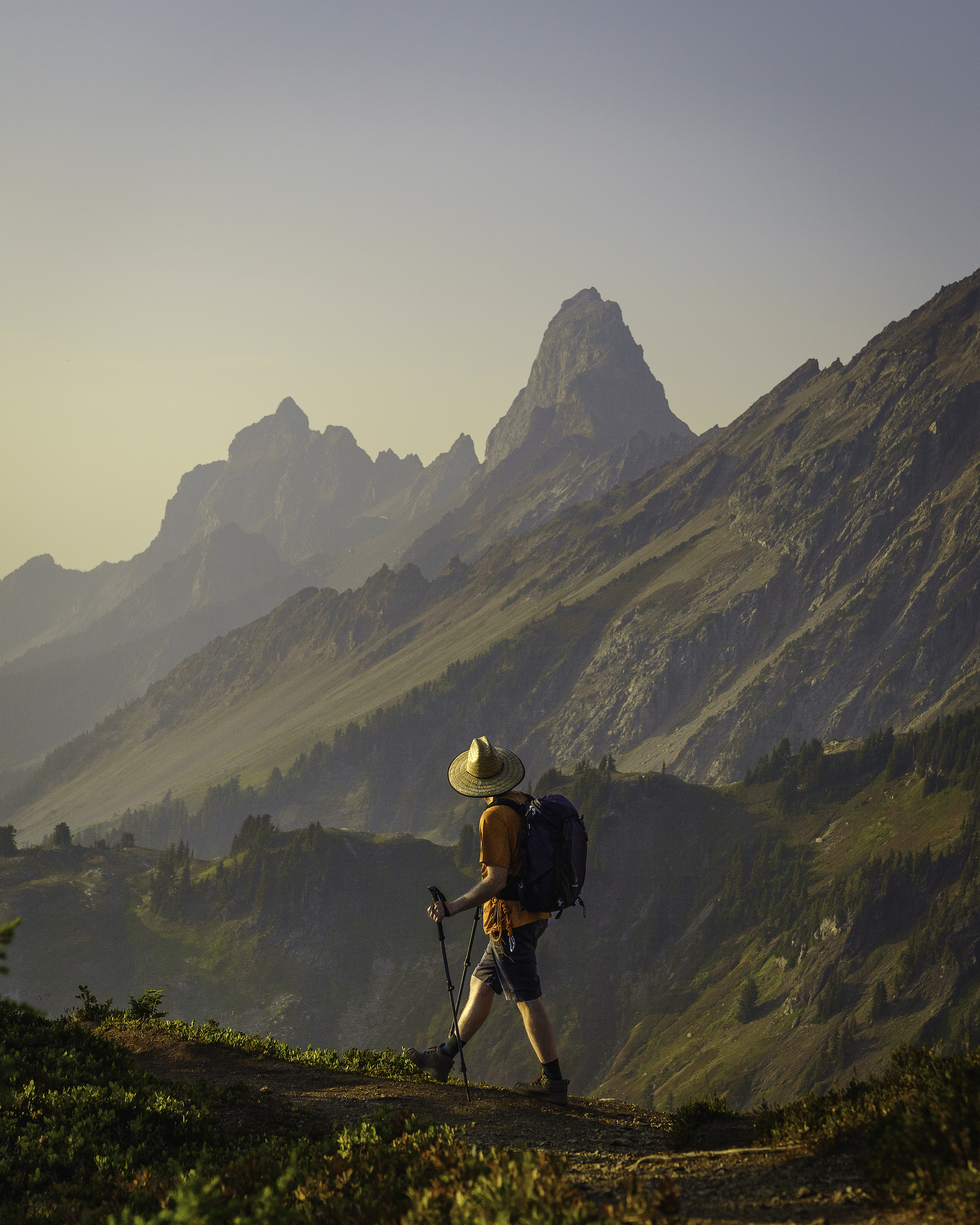 2nd hikers in action Patryck Ignaciuk A hiker wearing a broad hat hikes in front of pointy mountain peaks.