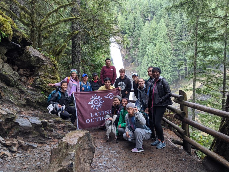 A Latino Outdoors hiking group poses for a photo next to a waterfall.