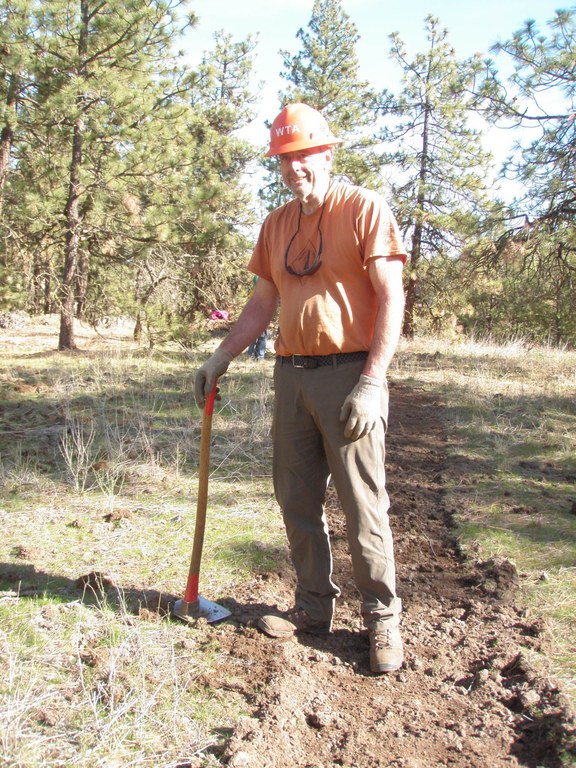 Alan Alan stands on trail with a grub hoe in one hand.
