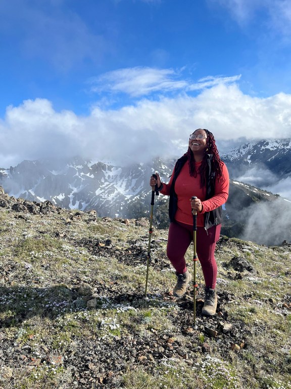 Angelic smiling, holding hiking poles while on a hike. Photo by Angelic Friday.
