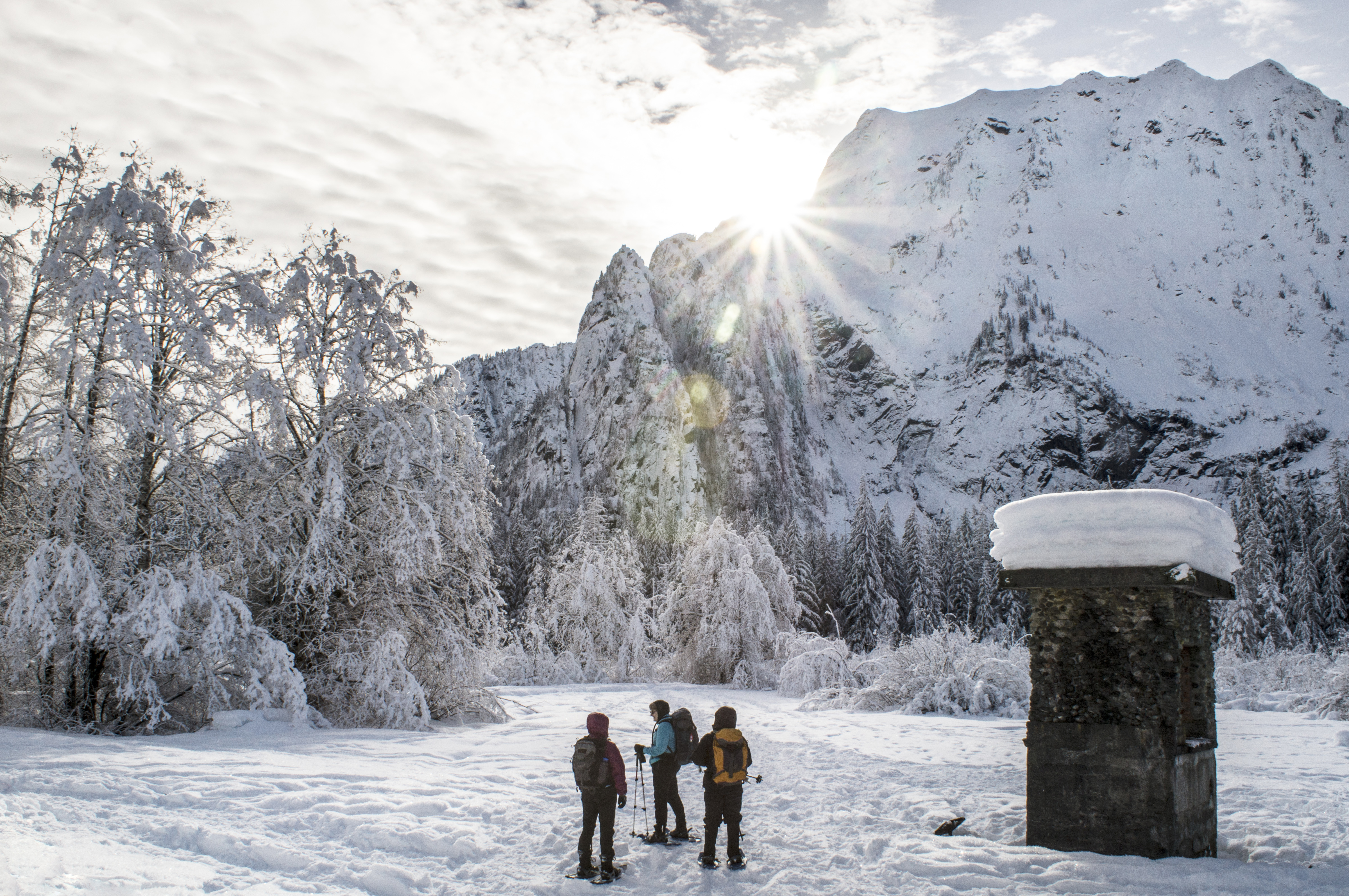 Big Four Snowshoe Photo by Heidi Walker Three snowshoers pause on trail at the base of a montain. Snowly landscape and some kind of chimmney structure in background.