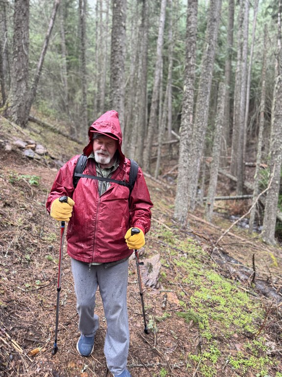 A hiker in a red rain coat walks on trail.