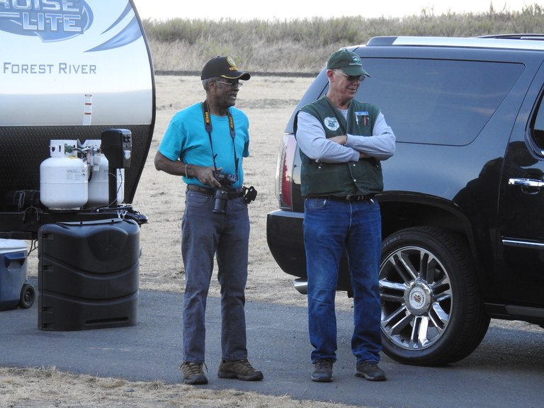 Two folks stand at the end of a trailer, one with a Washington State Parks vest on, the other holding a camera around their neck.