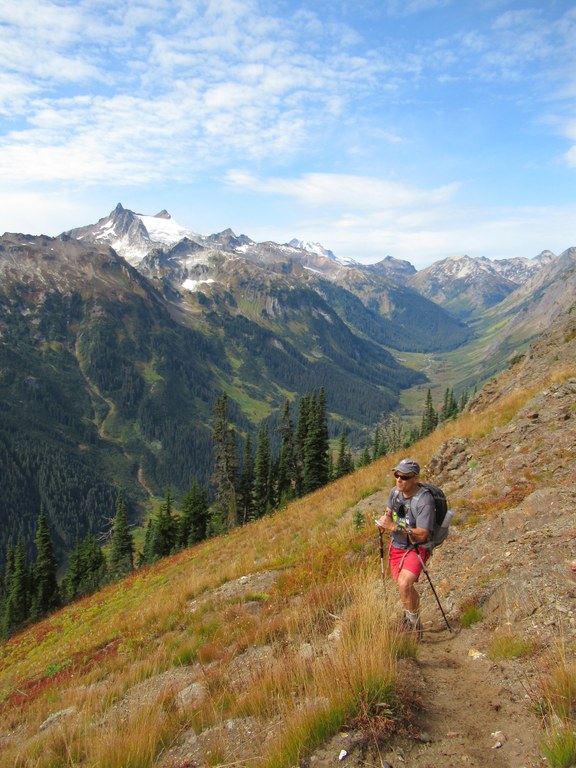 Craig Romano stands on Little Giant Pass with notepad in hand. A verdant valley lays below.