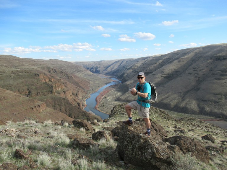 Craig Romano researches the Columbia River Gorge from a rocky outcrop. The Columbia winds below in an eroded canyon.