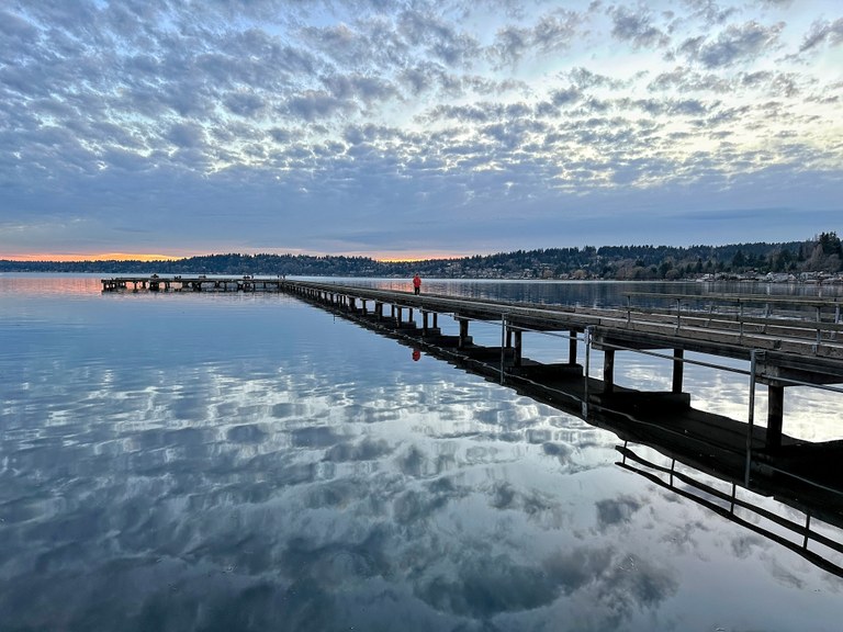 A dock extends onto a reflective lake at sunset.
