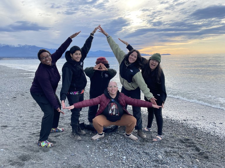WTA's Emerging Leaders Program cohort poses on the beach. Using their arms, they form a triangular shape in formation.