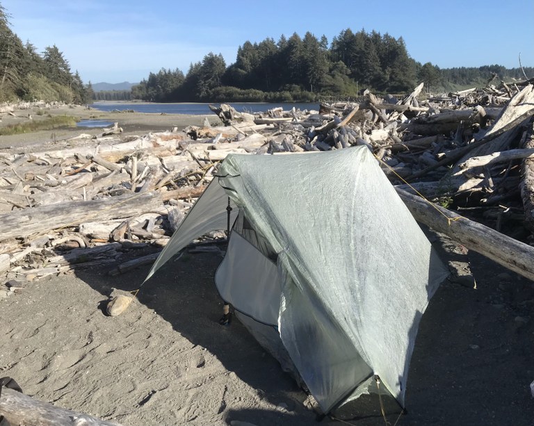 A single-walled shelter is pitched on the sand of a beach.