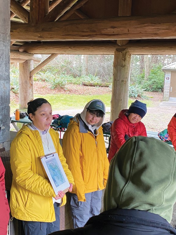 Valeria Santiago preps community partners for an activity focused on the Salish Sea for her independent project. Photo by MJ Sampang A hiker gives a presentation to a group from under a wooden pavilion.