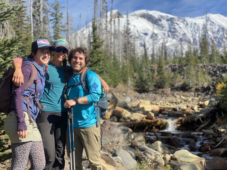 Three friends smiling in front of Mount Adams, mountain and creek in background.