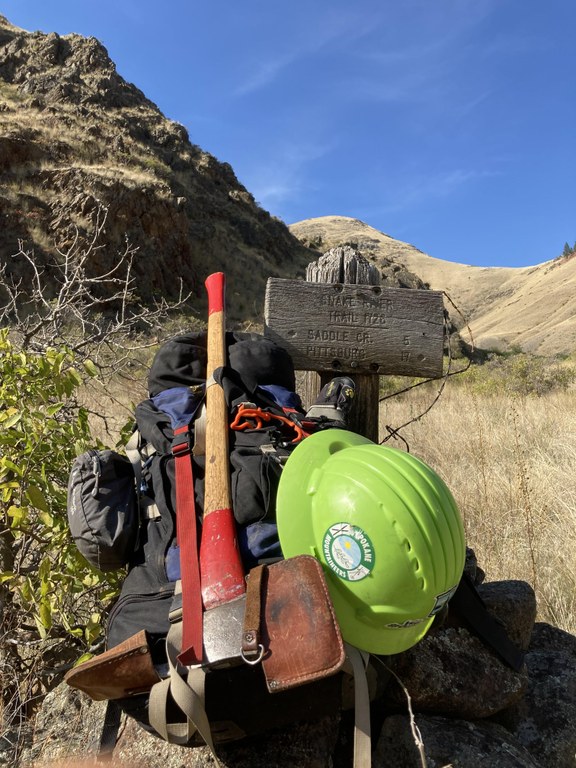 The Pulaski is worth its weight for backcountry trips. Photo by Holly Weiler. A Pulaski is strapped to a backpack. A hard hat hangs next to it.
