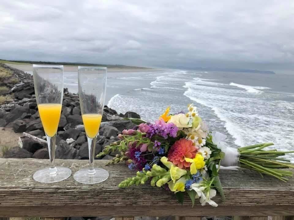 Two flutes with drinks and a bouquet of flowers with the coast behind them. Photo by Ashton Weis.