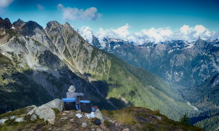 A hiker rests on their hiking chair looking out at mountain views.