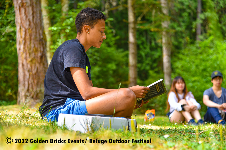 A person sits cross-legged on grass reading.
