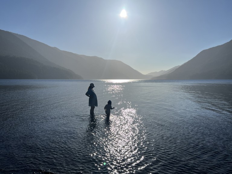 A pregnant adult standing in a lake with a young child. 