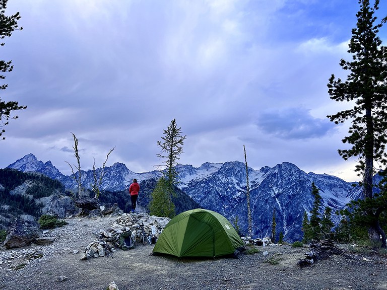 A hiker looks out forest from a high campsite. 