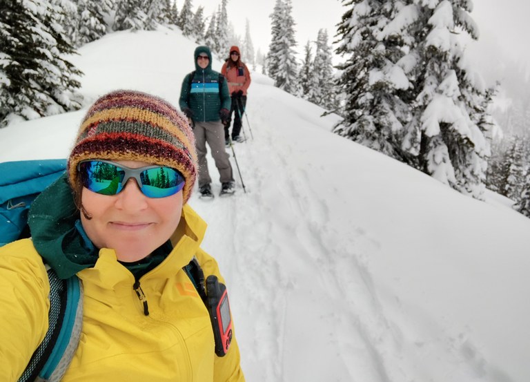Selfie of hiker in winter gear with two snowshoers behind her.