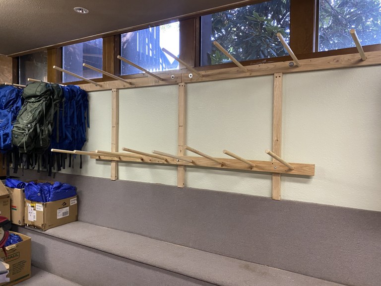 Pierce Country Gear library backpack racks Wall of wooden pegs for backpack storage. Window above pegs. Green and blueovernight backpacks to the left of image.