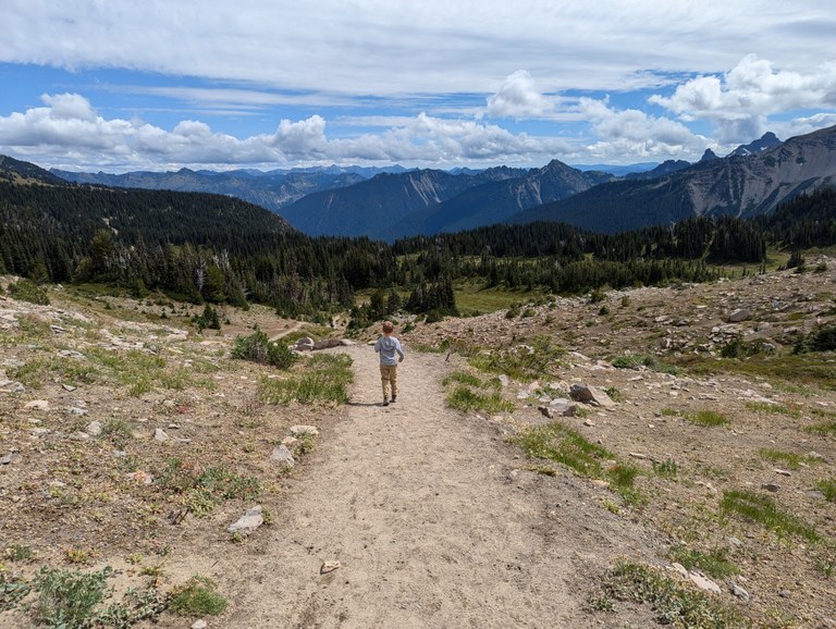 Sunrise Rim Loop A toddler hikes on a wide trail with views of rows of peaks in the distance.