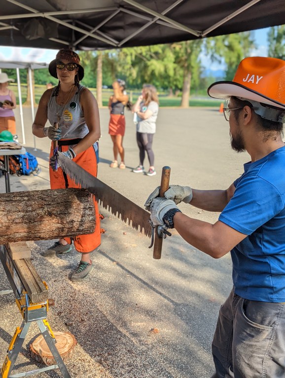 Many folks got to try out a crosscut saw at the Refuge Outdoor Festival — and even got to take home a souvenir! Photo by Zachary Toliver. Two people use a crosscut saw at a demonstration. Each person holds one end of the saw to work in tandem.