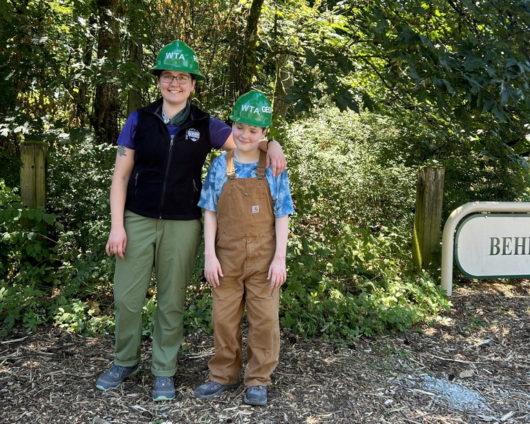 Two youth volunteers stand in the tanbark at a city park.
