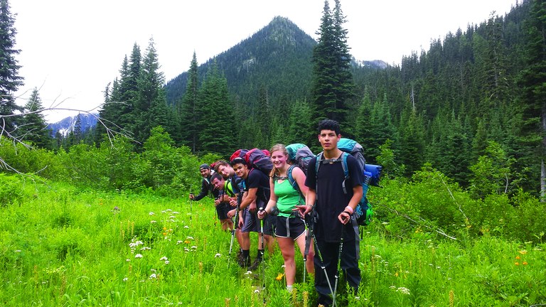 A group of youth backpackers hike near a meadow.